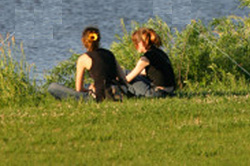 two girls sitting at bank of river, with back to camera 