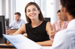 Woman sitting at computer talking to man