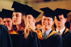 univeristy students in graduation gowns and hats seated and smiling