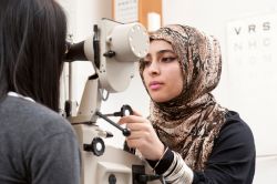 female using optometry machine to examine another female's eyes