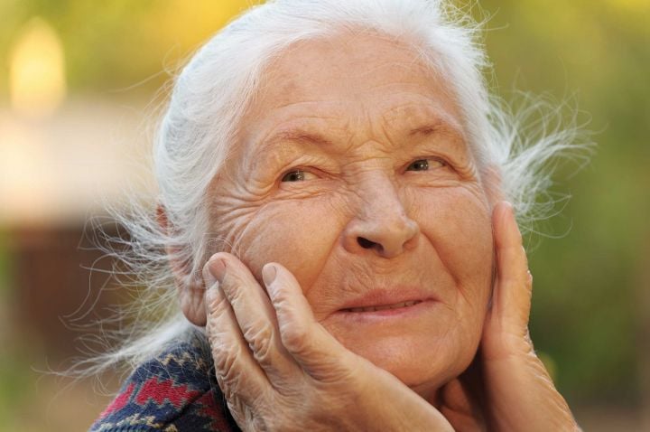 Older woman with hands on face, smiling.