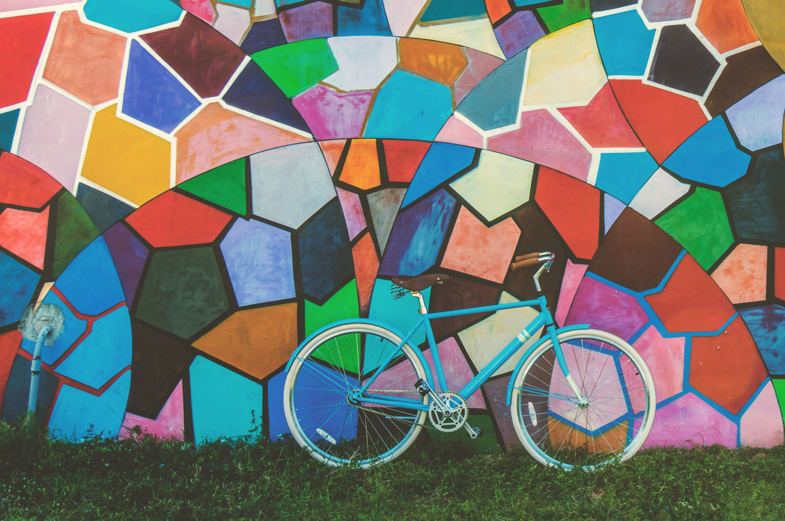 Blue bicycle on grass leaning against a colourful mural wall in a mosaic design