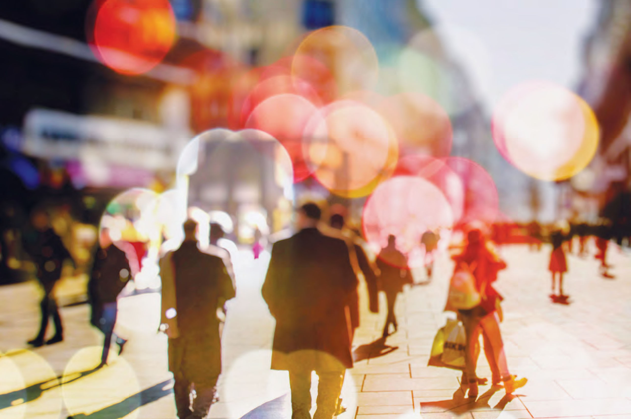 Partly blurred image of people walking in a paved public square with brightly coloured lens flare