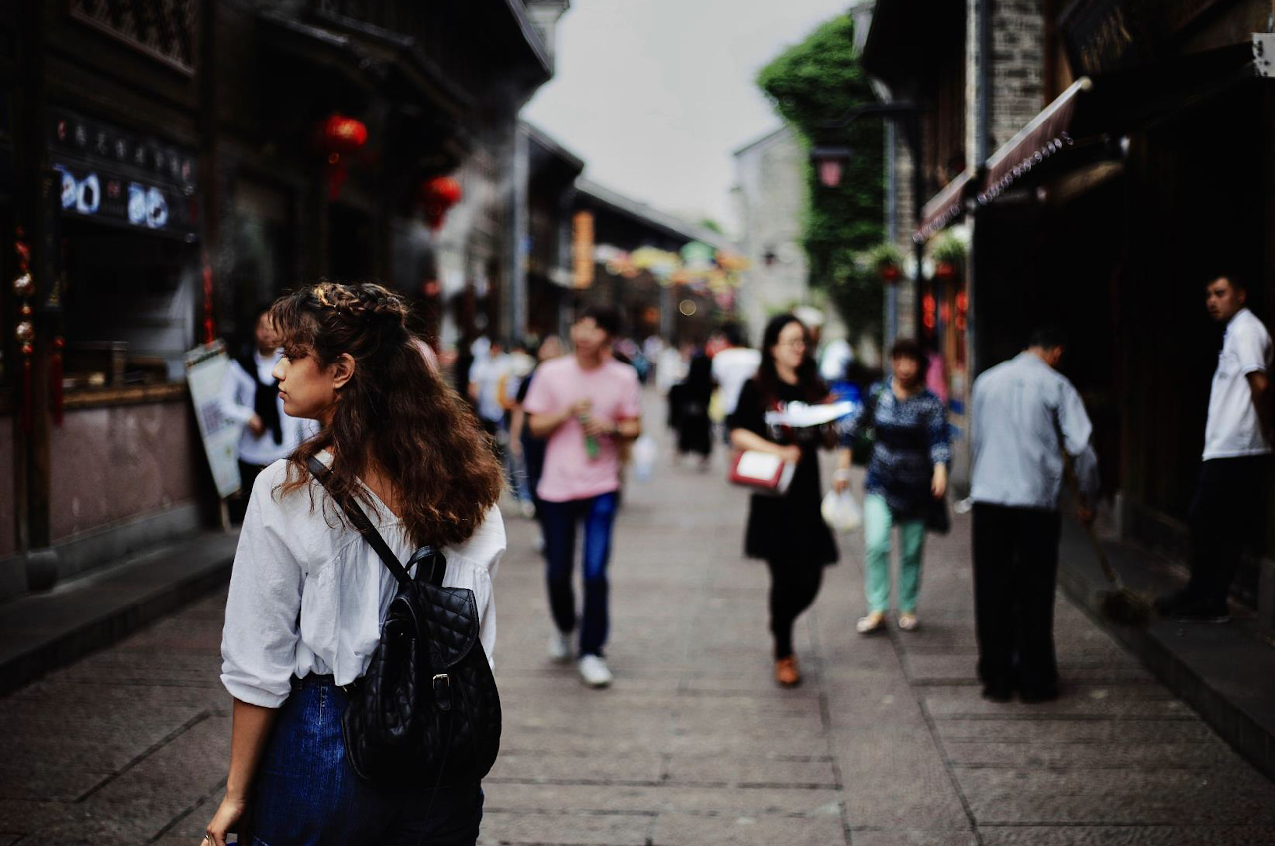 People walk down an old-style narrow shopping street in an Asian city