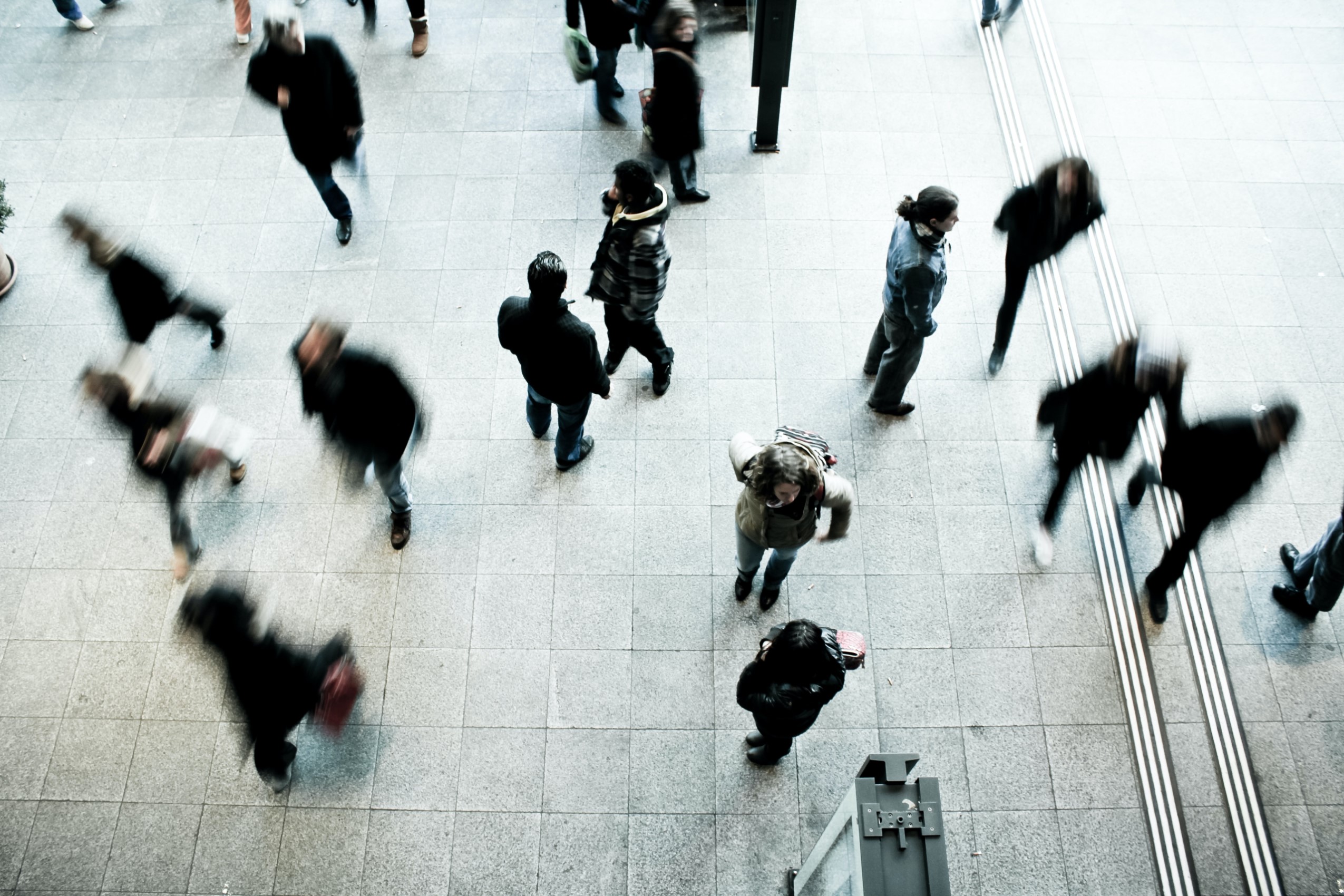 A blurred crows of people walk through a public space like a train station