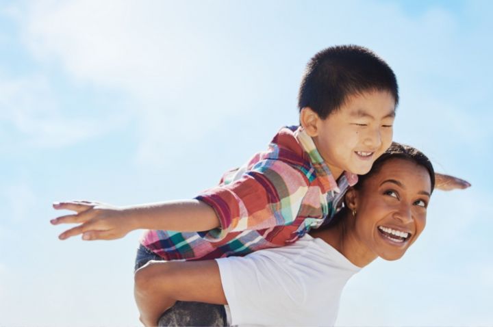 Kid in a checked shirt getting a piggy back ride from a smiling adult