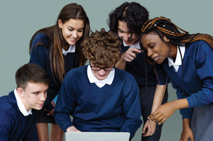 Five teenagers in school uniform, crowded around a laptop, while one types