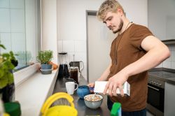 A man in a kitchen pouring milk into a bowl of cereal
