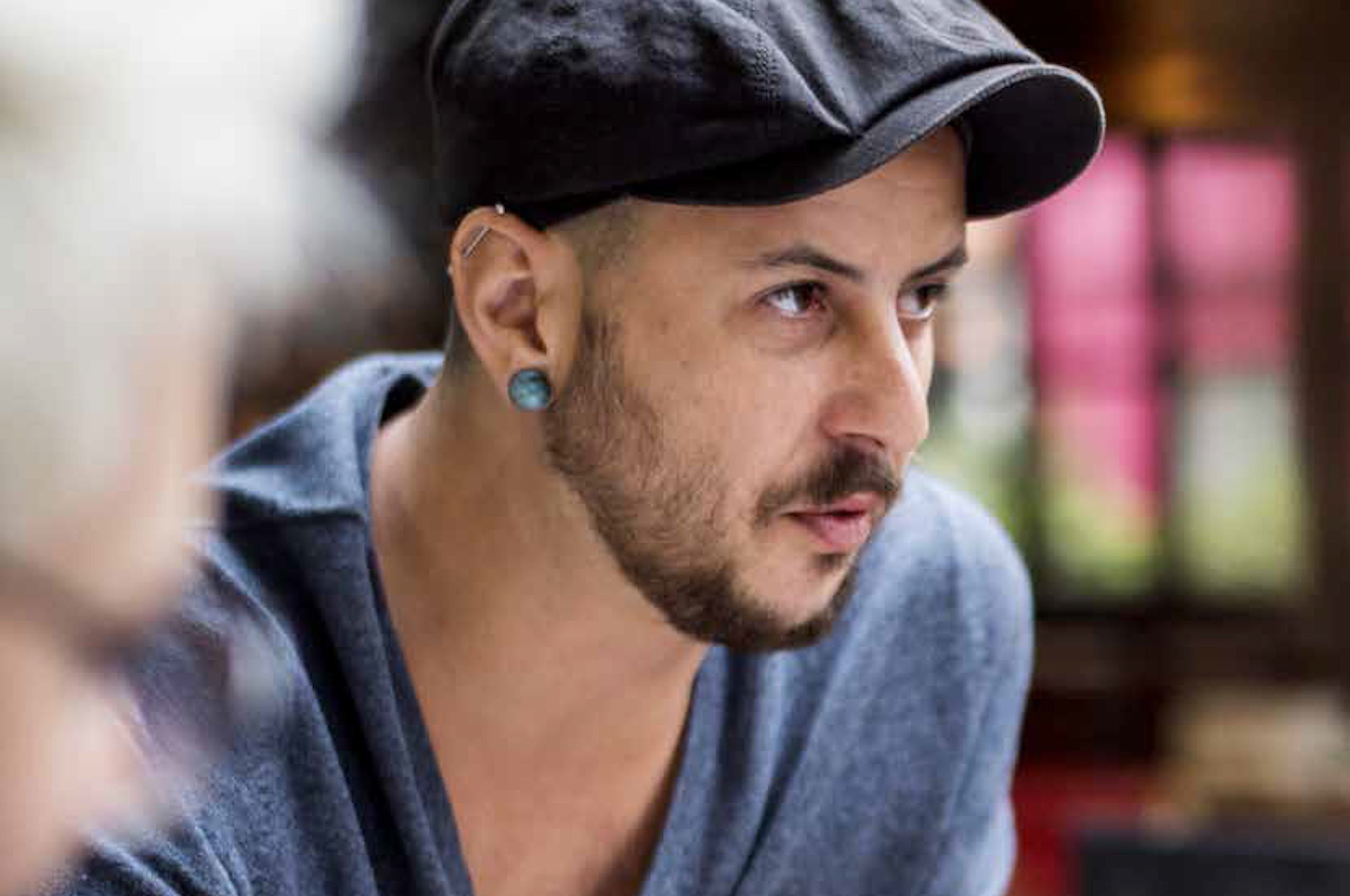 Bearded person with baker boy cap, large blue pearl earring and bar piercing 