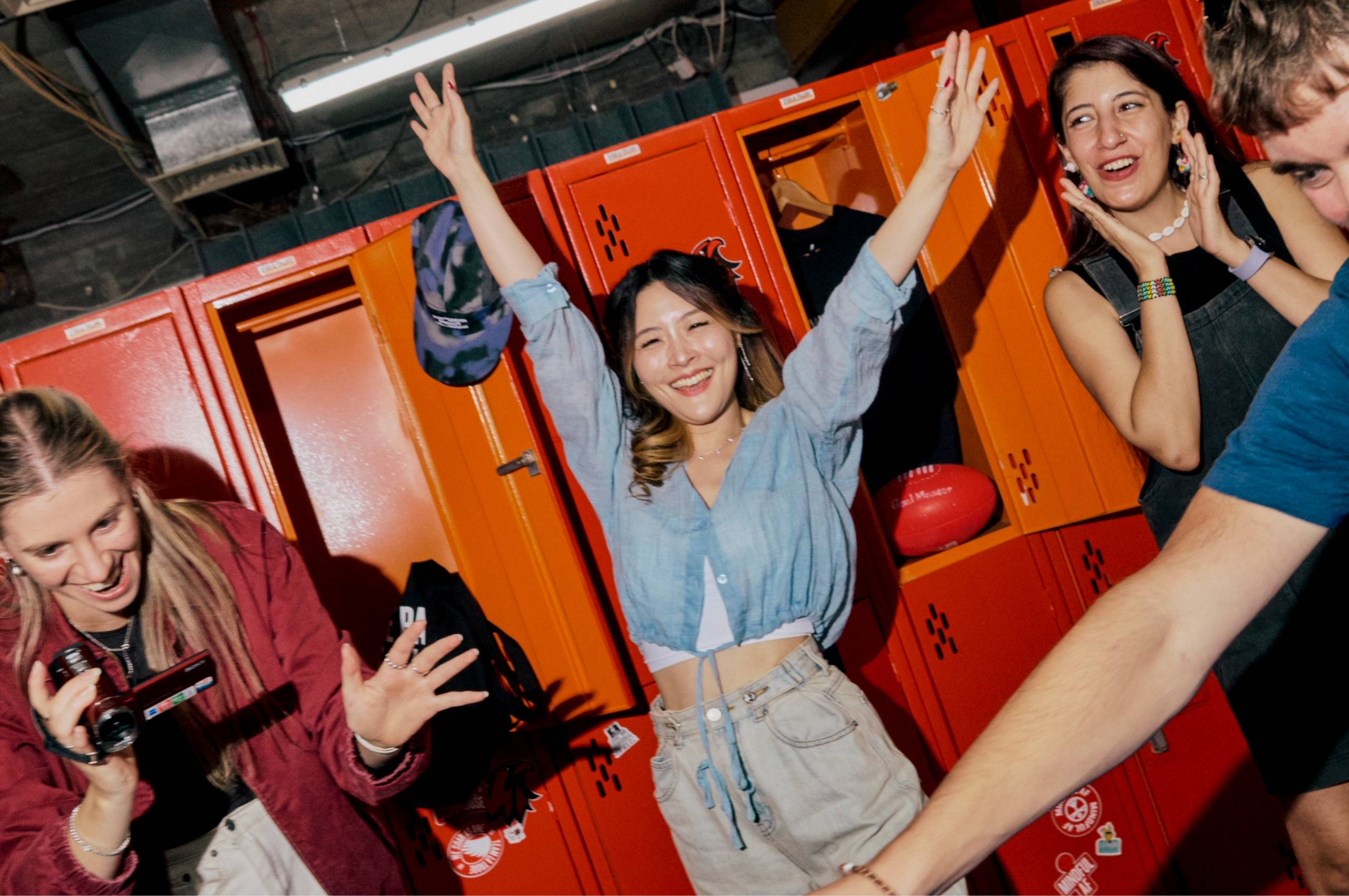 Group of students laugh and celebrate together in front of bright orange lockers.