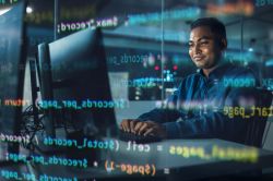 Professional working at a computer with programming code displayed.
