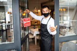 male in apron at hospitality venue changing window sign to 