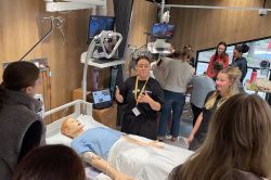 Instructor teaching students around a patient mannequin in a medical simulation lab.