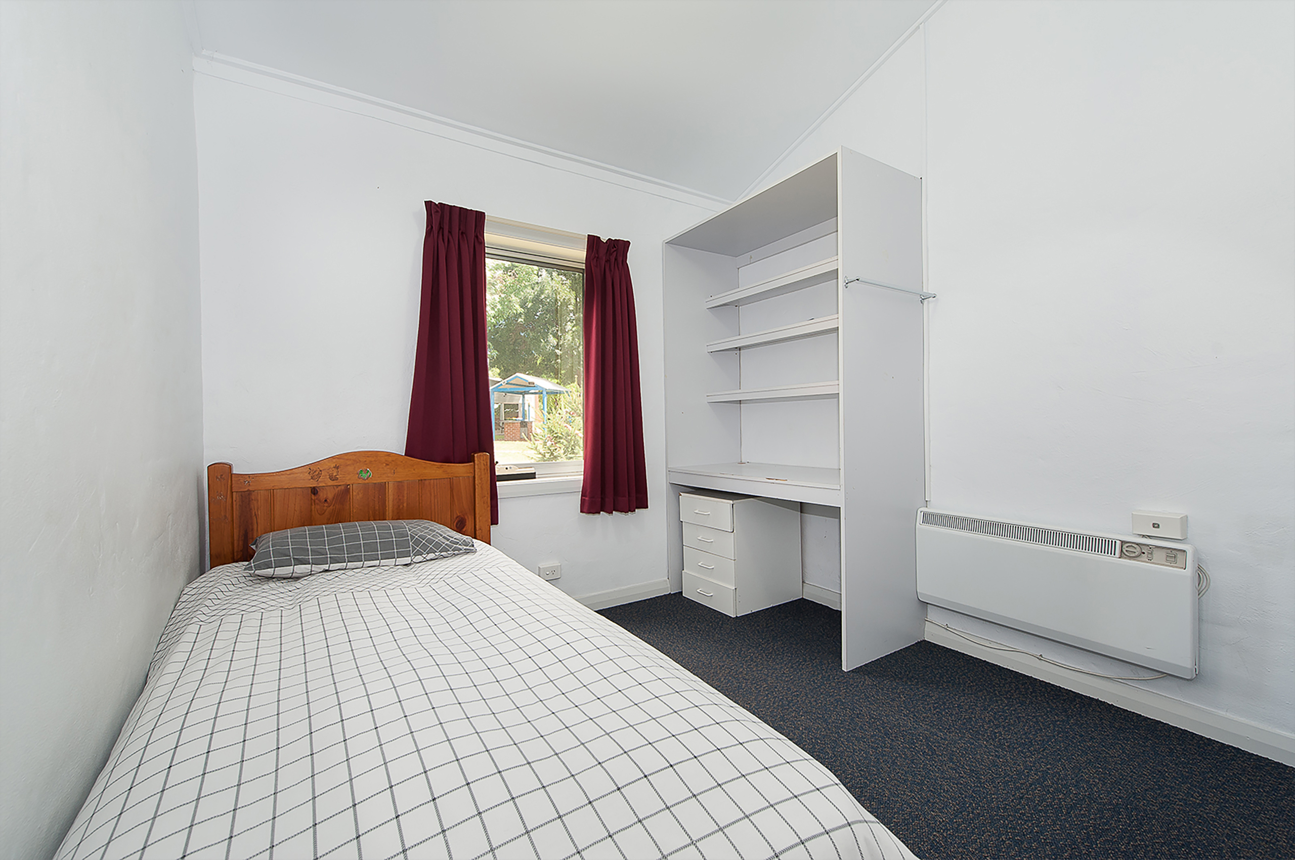 Single bed student accommodation with a heater, shelves and drawers.