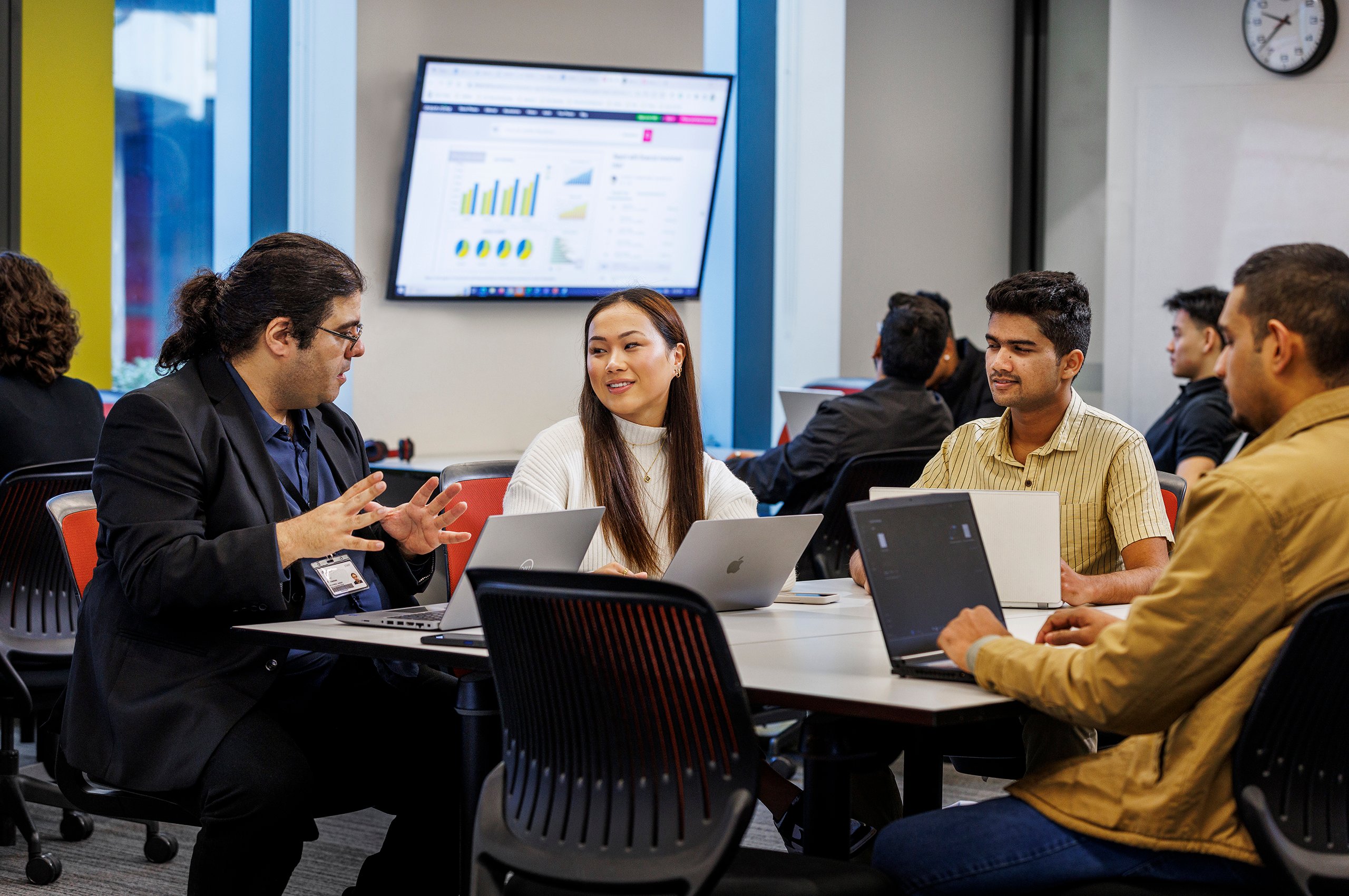 A La Trobe tutor speaking to students sitting at a table in a classroom.
