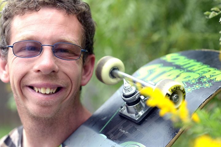 Close crop of a Man smiling, with a skateboard over his shulder