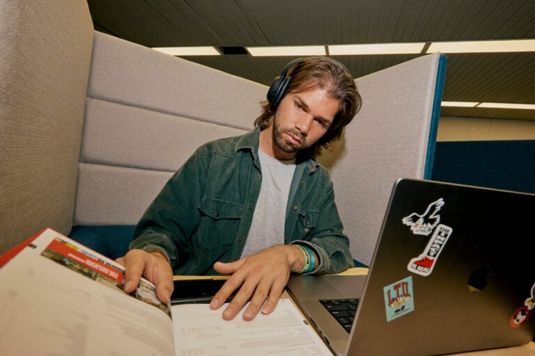 A student studying in the library with their laptop and notebooks