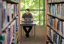 A student sitting at their laptop in between bookshelves