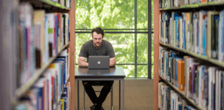 A student sitting at their laptop in between bookshelves