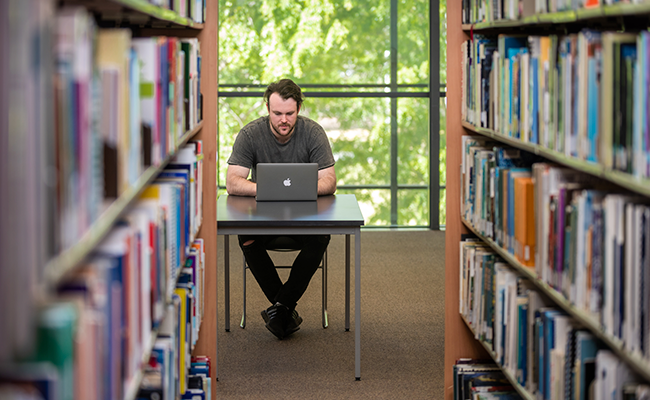 A student sitting at their laptop in between bookshelves