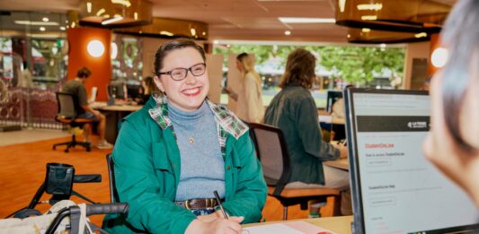 A student sitting with a notebook talking to ASK La Trobe in the Library