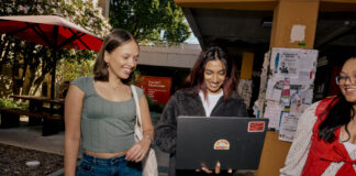 Three students walking and looking at a laptop