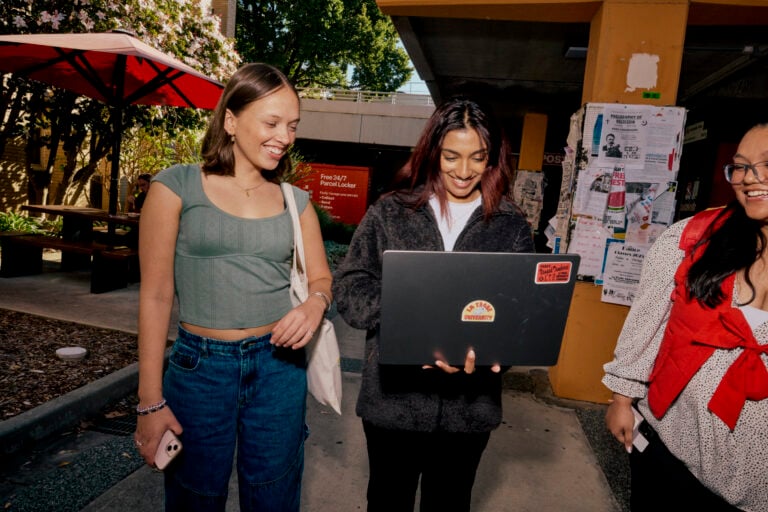 Three students walking and looking at a laptop