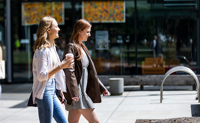 Two students walking and one is holding a coffee