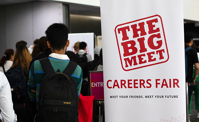WordPress Article (650 x 400) Student walking into Big Meet event standing next to a banner with the words 'The Big Meet Careers Fair' displayed