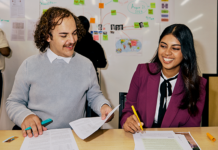 Two students sitting and working at a table. They are highlight pieces of paper.