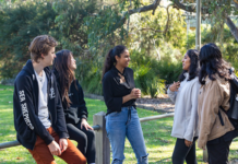 A group of students standing outside in a group having conversation and laughing