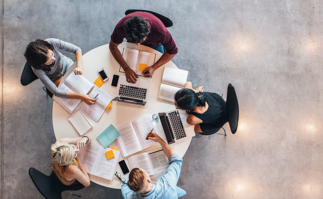 Students sat around a table studying with laptops and notes