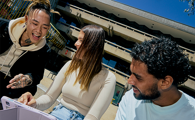 A group of three La Trobe students smiling and having conversation at a table