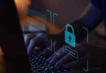 Someone typing on a laptop in the dark, with a blue lock symbol on top.