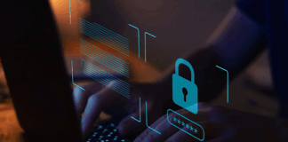 Someone typing on a laptop in the dark, with a blue lock symbol on top.