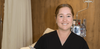 A student in a nursing uniform holding a file next to a hospital bed