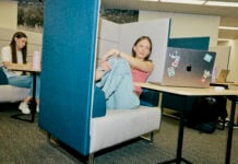 Student looking at their laptop in the library, surrounded by other students