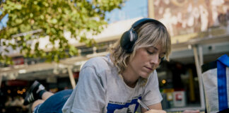 A student lying on the lawn in the Agora writing in a notebook.
