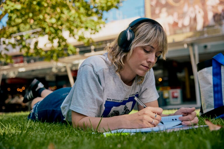 A student lying on the lawn in the Agora writing in a notebook.