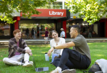 A group of three students sitting on the lawn outside the Bundoora library.