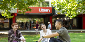 A group of three students sitting on the lawn outside the Bundoora library.