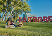 Students sitting on the grass by a large La Trobe letter sign