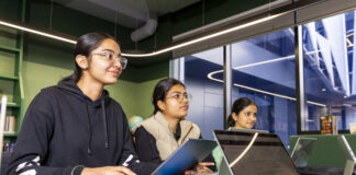 Three students sitting with their laptops at a table.