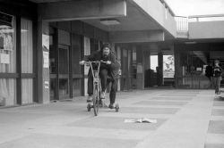 Dave Lindsay, riding a large tricycle in the Agora, La Trobe University, Bundoora. Date  August 1970