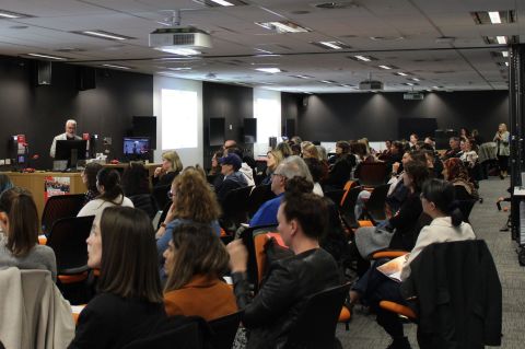 A large group of people seated in chairs, engaged in discussion within a spacious room
