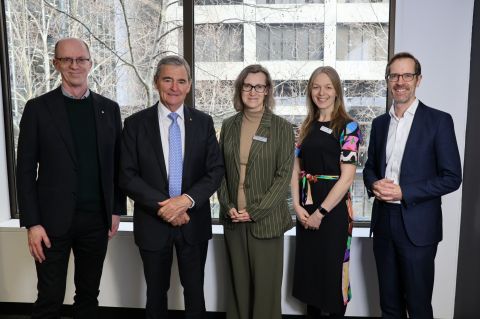 Five people standing together in front of a large window, with natural light illuminating their faces