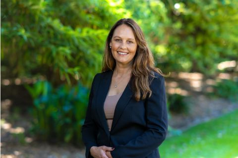 A woman in a suit and tie stands confidently in front of a backdrop of trees