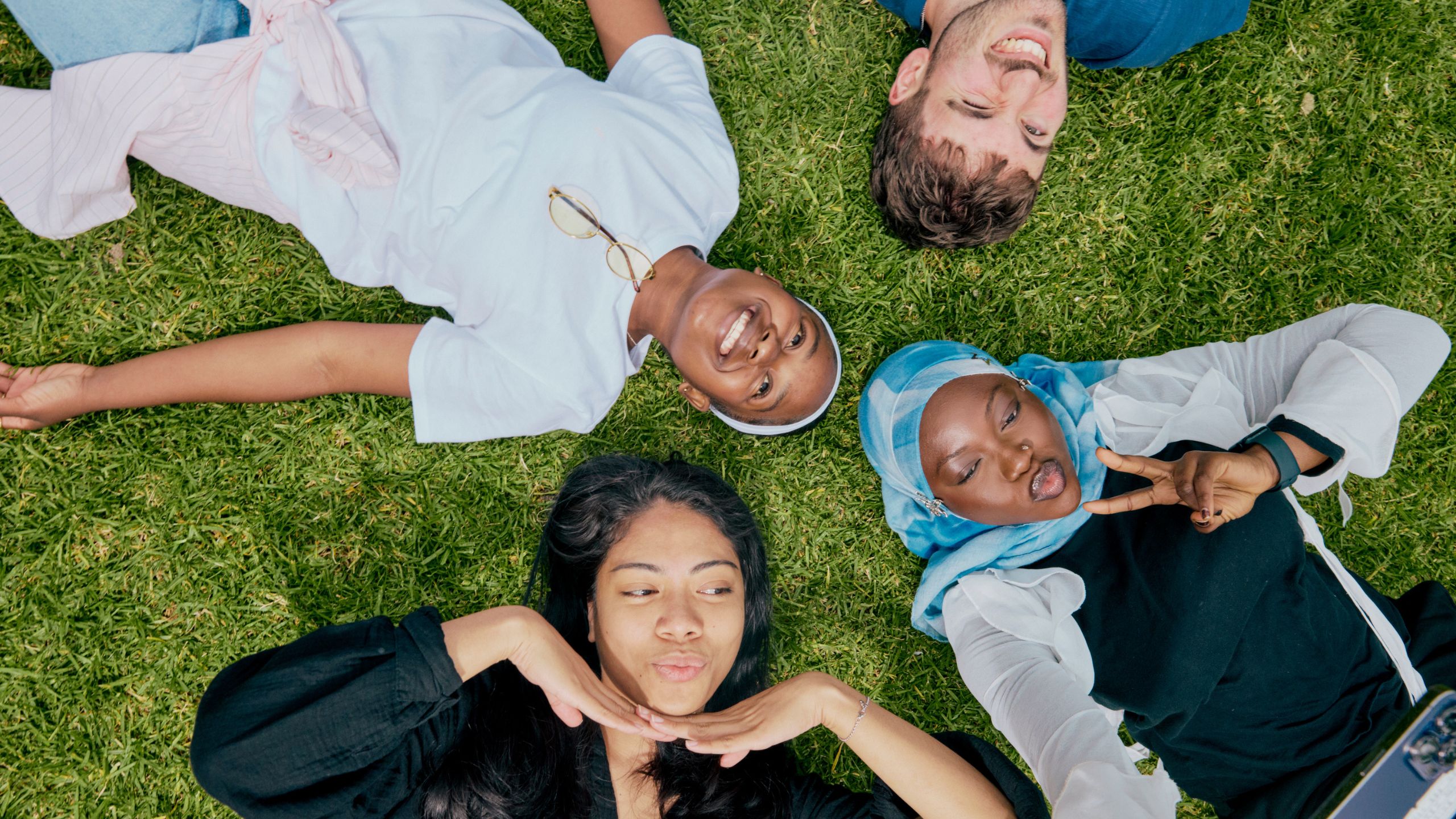 Students lying on the lawn, smiling and posing for a selfie.