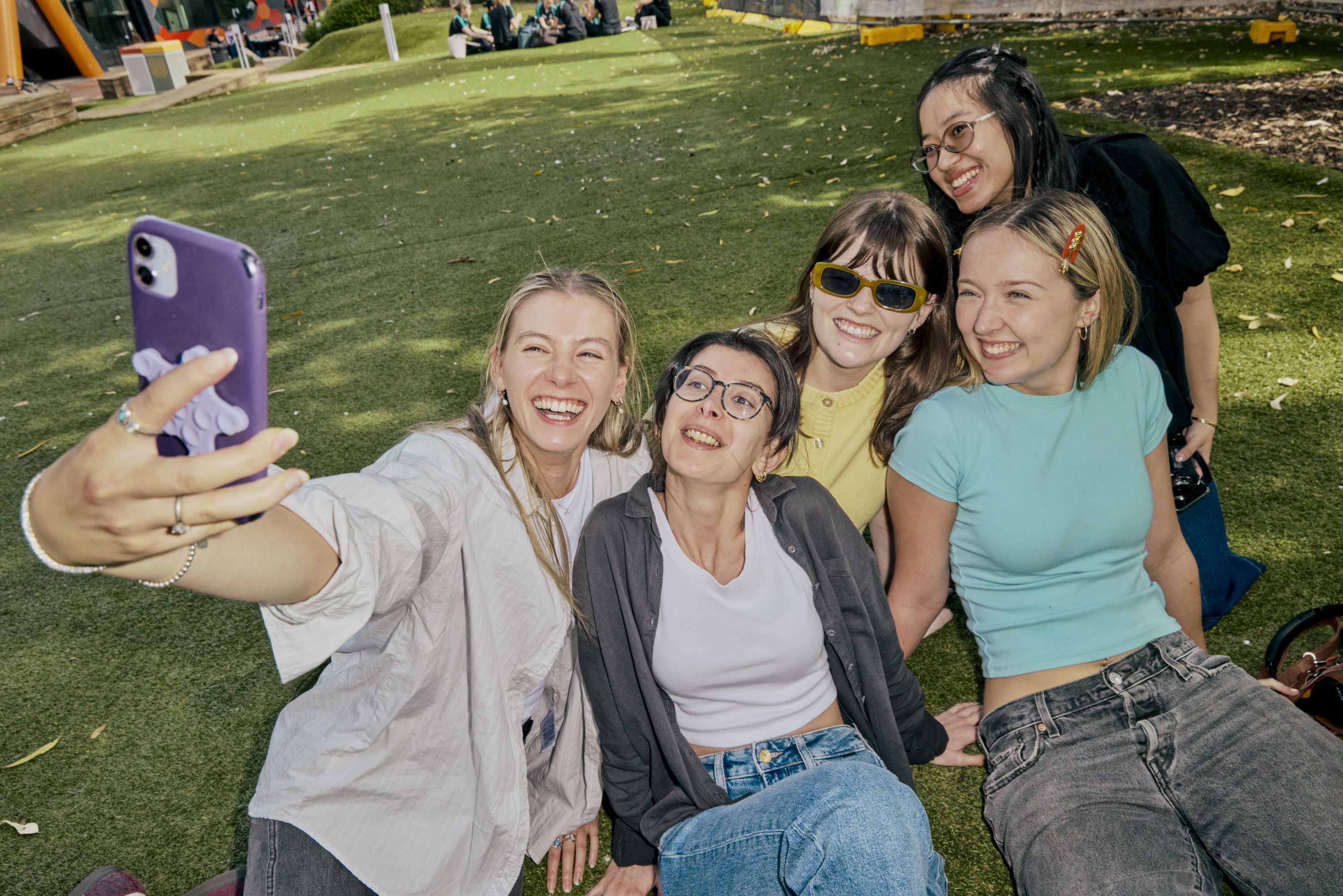 A group of students smiling and posing together with their phone on campus