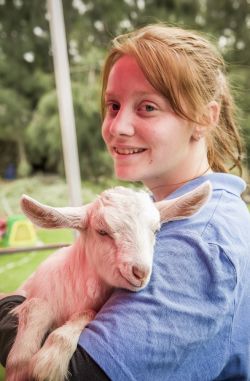 female smiling at camera holding white baby goat